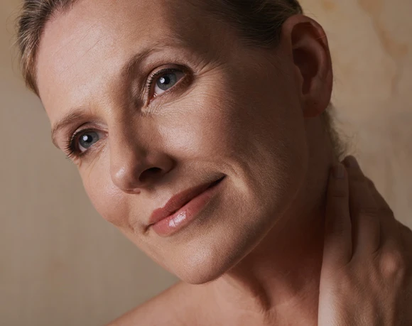 Close-up portrait of a mature woman touching her neck and looking upward with a soft expression