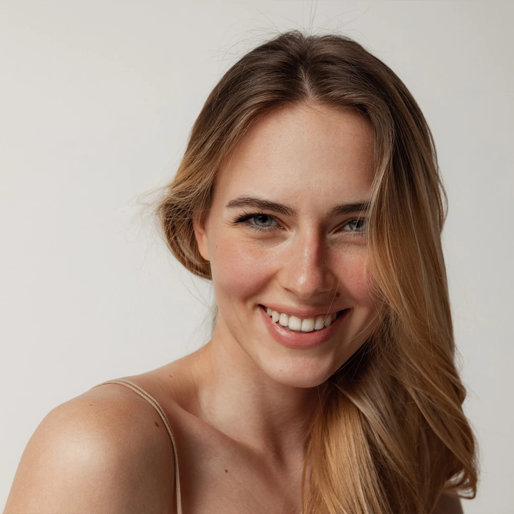 Close-up portrait of a smiling young woman with long light brown hair against a soft neutral background